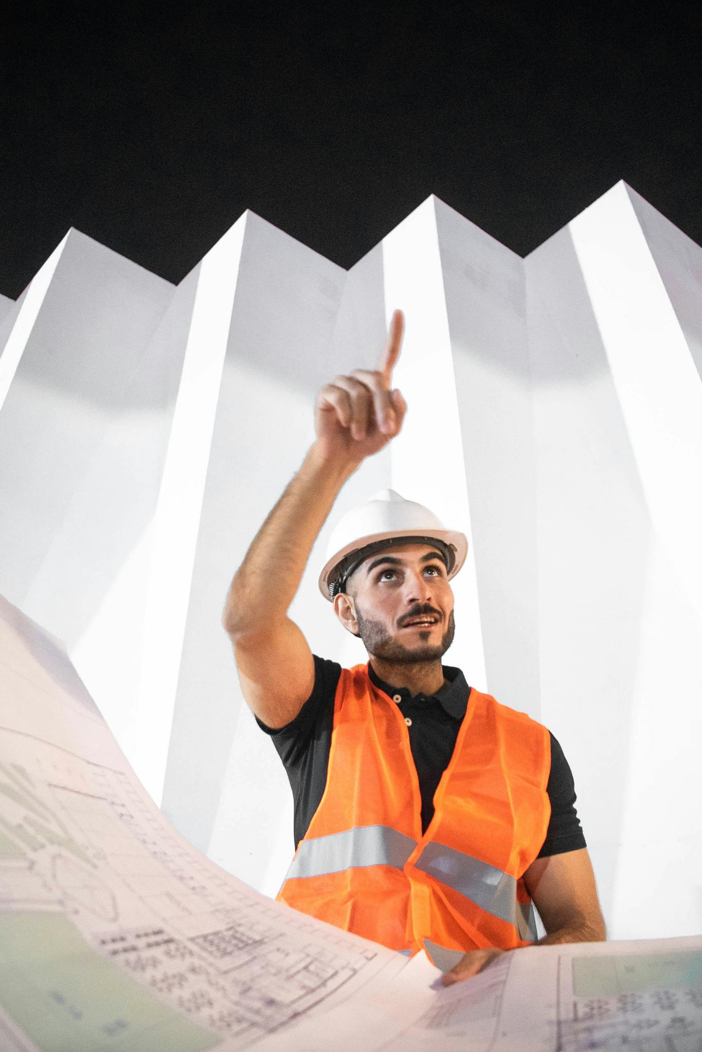 A construction worker in a helmet and vest analyzing blueprints under dramatic architecture.