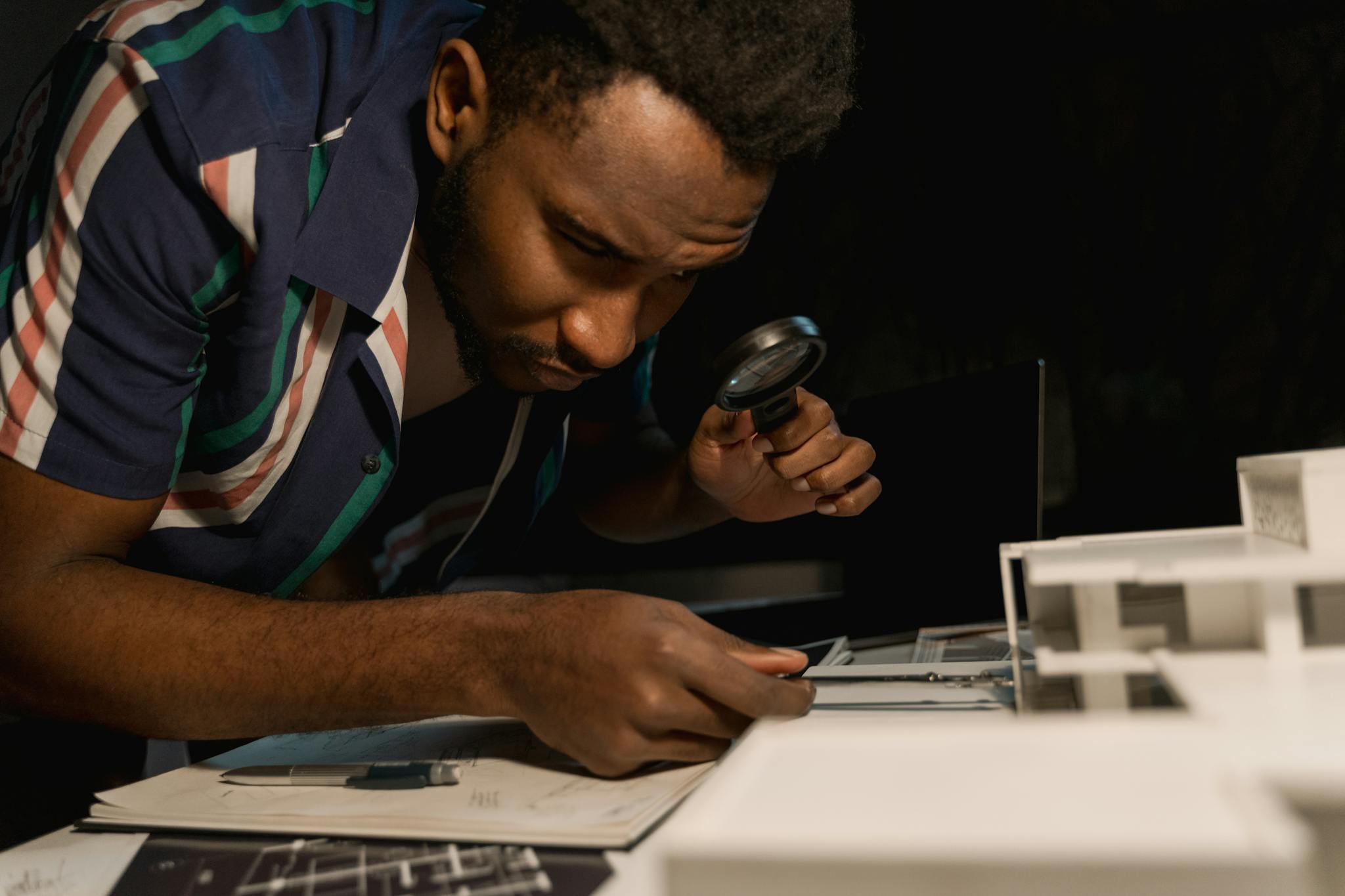 Architect intently examines a model with a magnifying glass, highlighting attention to detail.