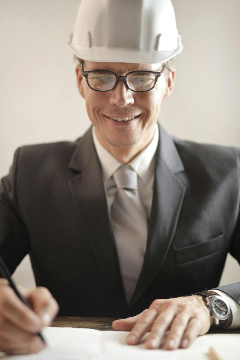 Male engineer in formal attire reviewing and signing construction documents indoors.