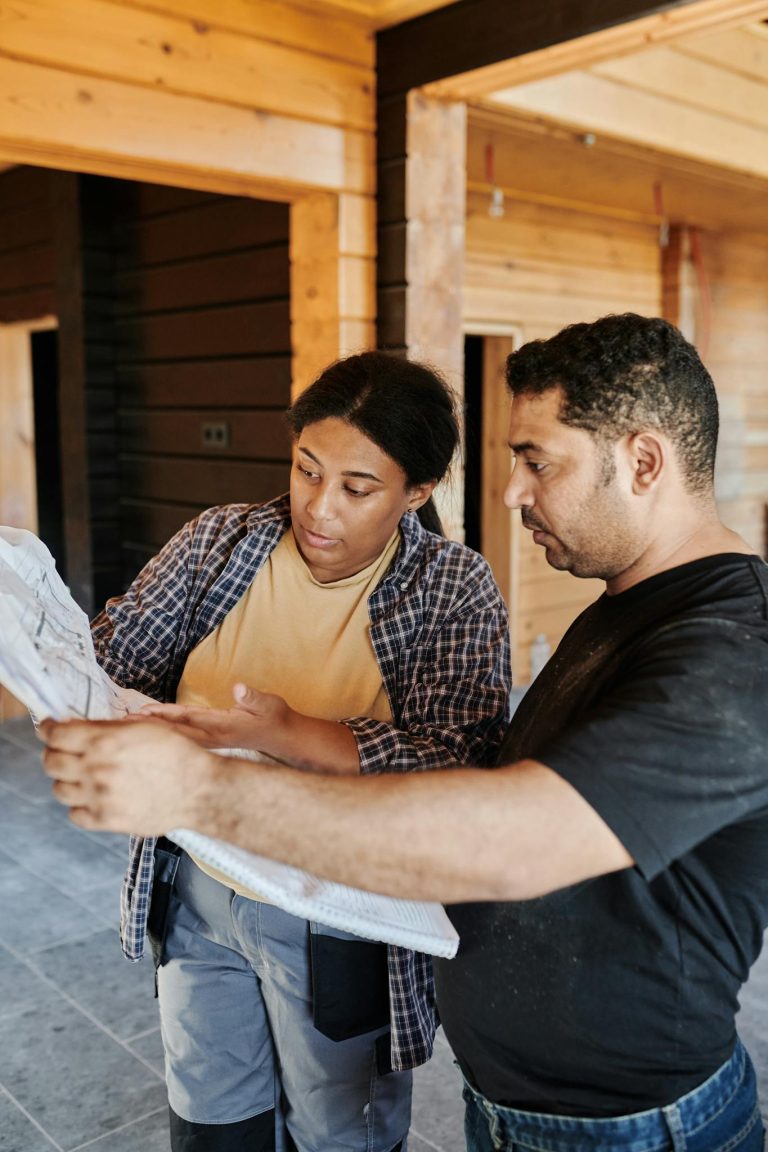 Two construction professionals examining blueprints in a wooden building interior.
